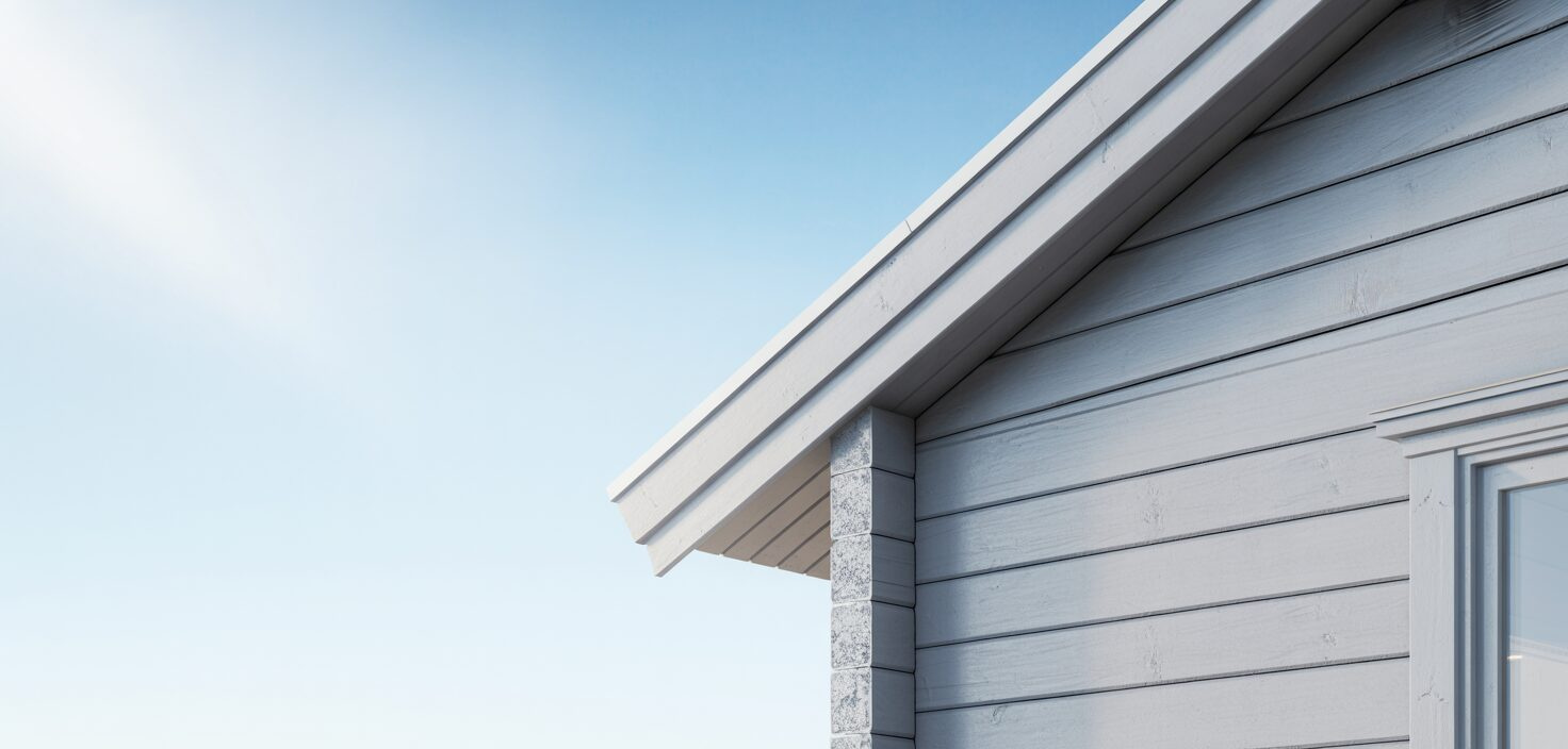 En solbelyst träfasad på ett hus målat i ljusgrått, med fokus på dess rena linjer och minimalistiska design.